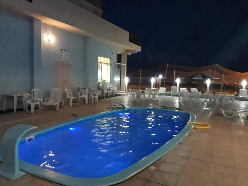 a large swimming pool at night with tables and chairs at hotel castelo in Cidreira