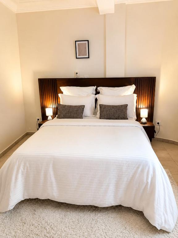 a bedroom with a large white bed with two lamps at Appartement cozy Bonamoussadi, WIFI & Goupe électrogène in Douala