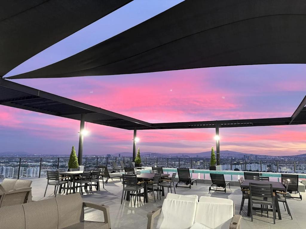 a rooftop patio with tables and chairs and a sunset at Depa con alberca cerca de Andares y Landmark in Guadalajara