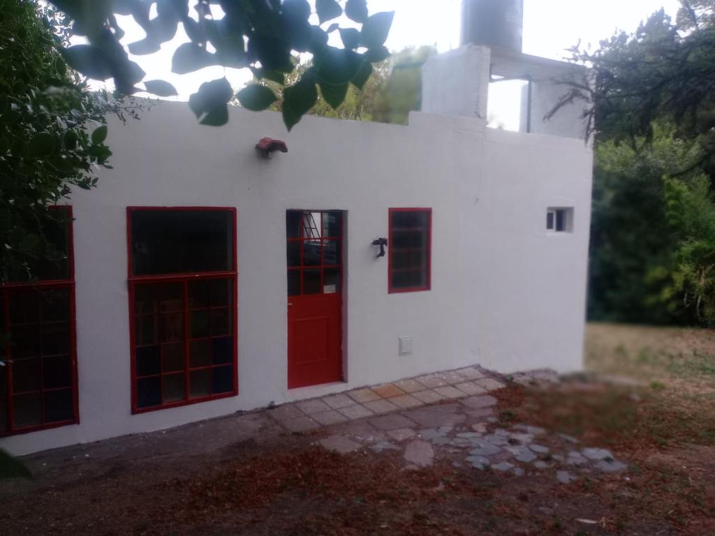 a white house with red doors and trees at La casita de Gorrión in Villa Ventana