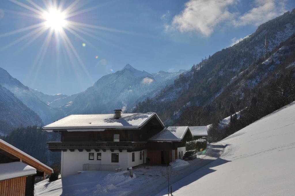 Apartments Obernosterer - Großglockner في كابرون: منزل في الثلج مع الشمس في السماء