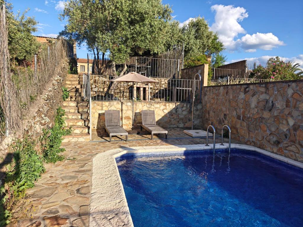 a swimming pool with two chairs next to a stone wall at Casa rural rio yeguas in Azuel