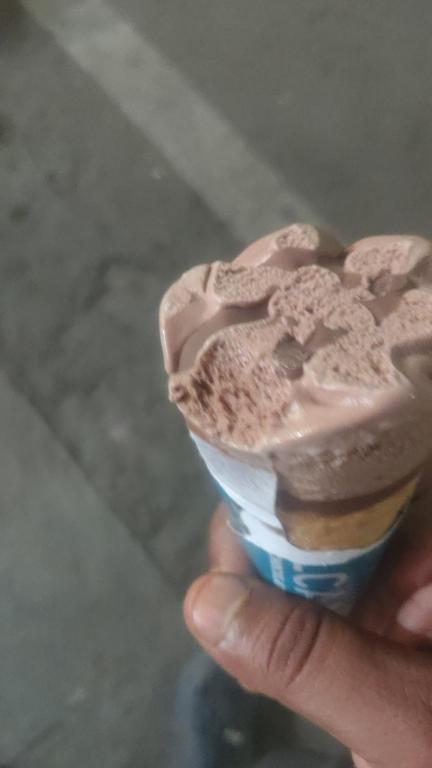 a hand holding a cupcake with chocolate frosting on it at Vipul in Kasrāwad