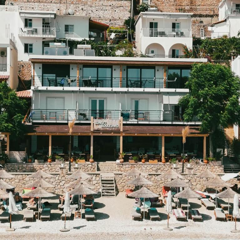 a hotel with tables and umbrellas in front of it at Sunset Boulevard Beach Hotel in Qeparo