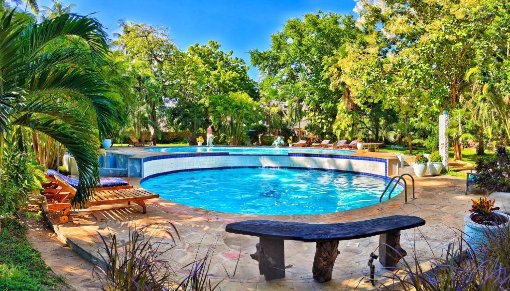 a large swimming pool with two benches and trees at The Garden Suite in Mtwapa
