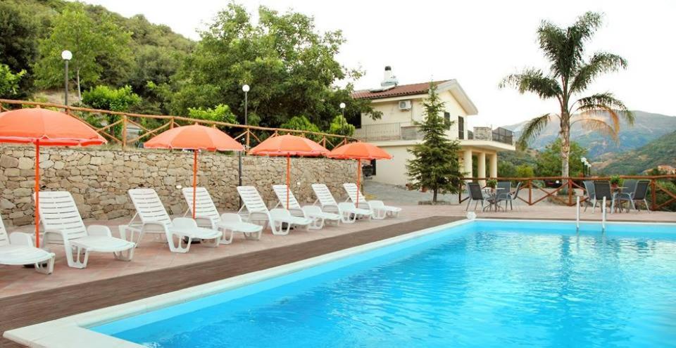 una piscina con sedie e ombrelloni accanto a un edificio di La Parrinara a Francavilla di Sicilia