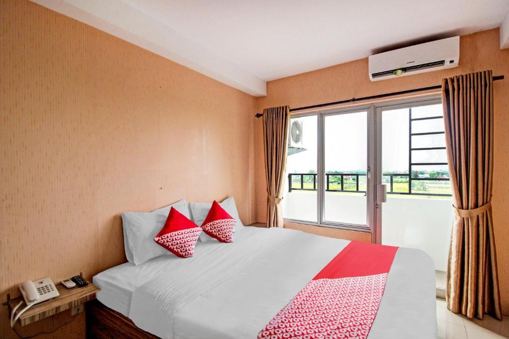 a bedroom with a bed with red pillows and a window at Hotel O Tridasa in Medan