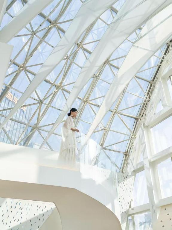 a woman in a white dress standing on a staircase in a building at Aspera Star Essence Sky Garden Panoramic Hotel-Jiefangbei Hongya Branch in Chongqing