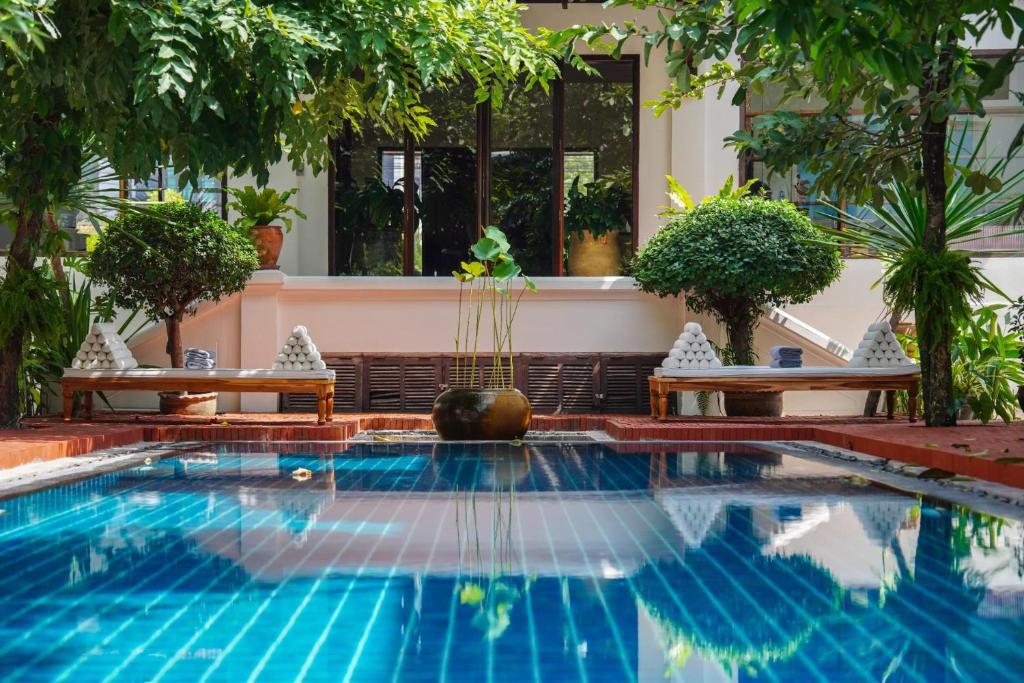 a swimming pool in a resort with two benches at Le Sen Boutique Hotel in Luang Prabang