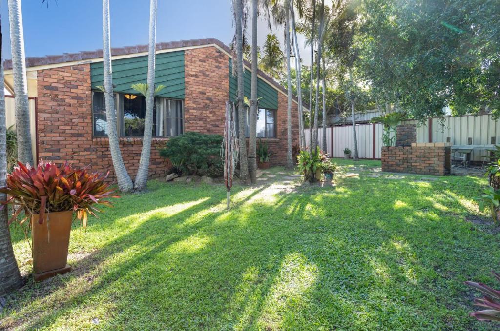 a backyard with palm trees and a brick house at Bromeliads in Iluka