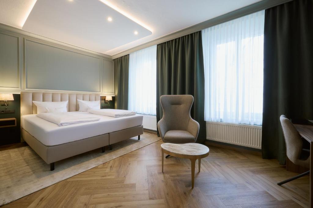 ein Schlafzimmer mit Bett, Stuhl und Fenstern in der Unterkunft Hotel Fletzinger in Wasserburg am Inn