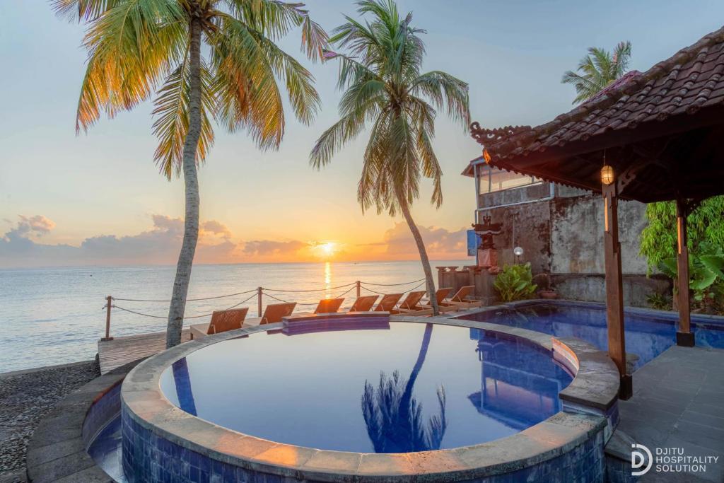 a swimming pool in front of the ocean with palm trees at Paradise Palm Beach Bungalows and Dive Center in Tulamben