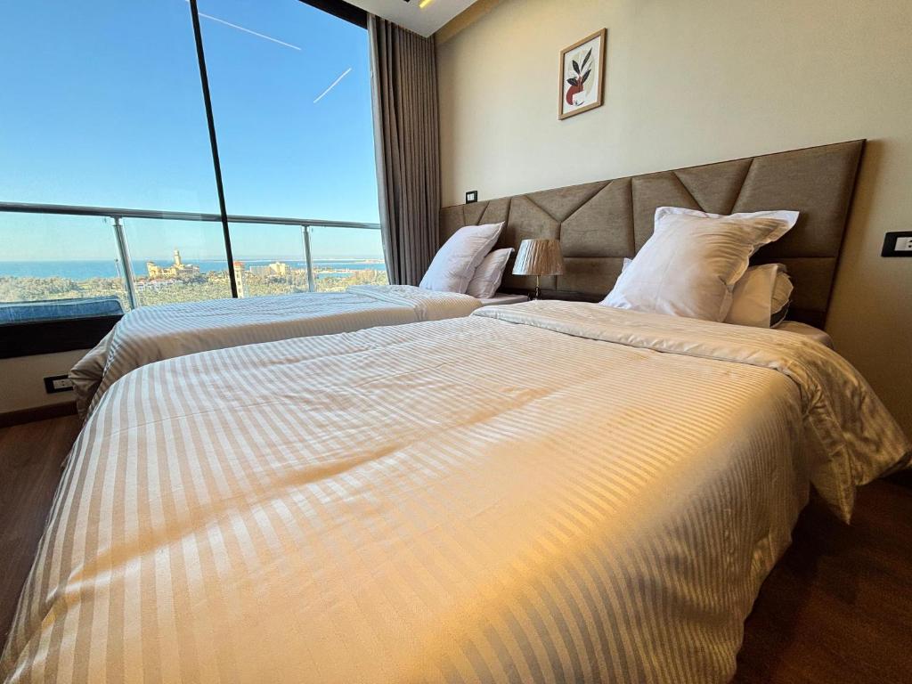 two beds in a hotel room with a large window at Azurea Suites in Alexandria