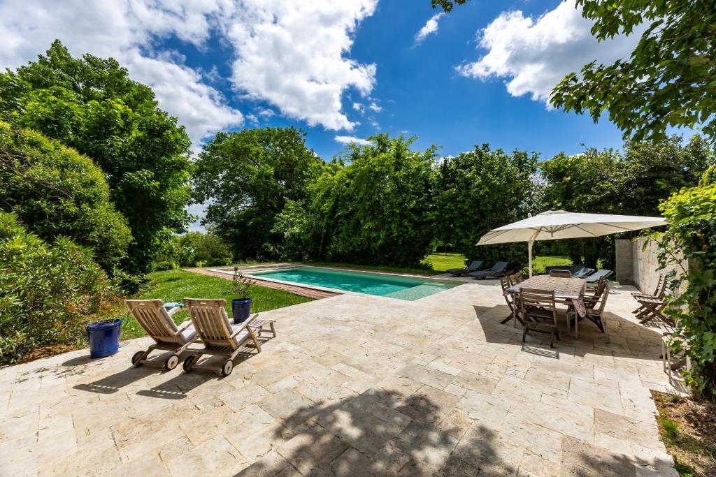 a patio with chairs and an umbrella next to a swimming pool at La Ferme - Château Le Noble in Saint-Germain-du-Puch