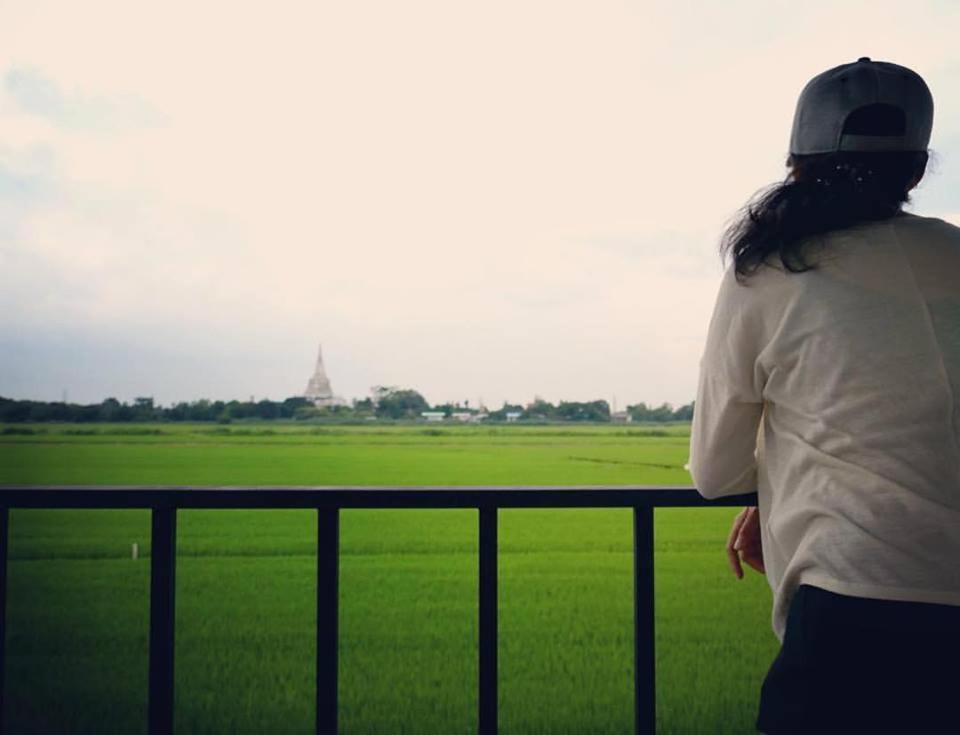 a woman standing on a fence looking at a green field at Slowlife House Ayothaya in Phra Nakhon Si Ayutthaya