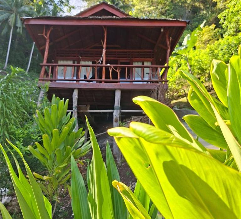 a wooden building with a balcony in a forest at Banua Guesthouse in Pulau Malenge