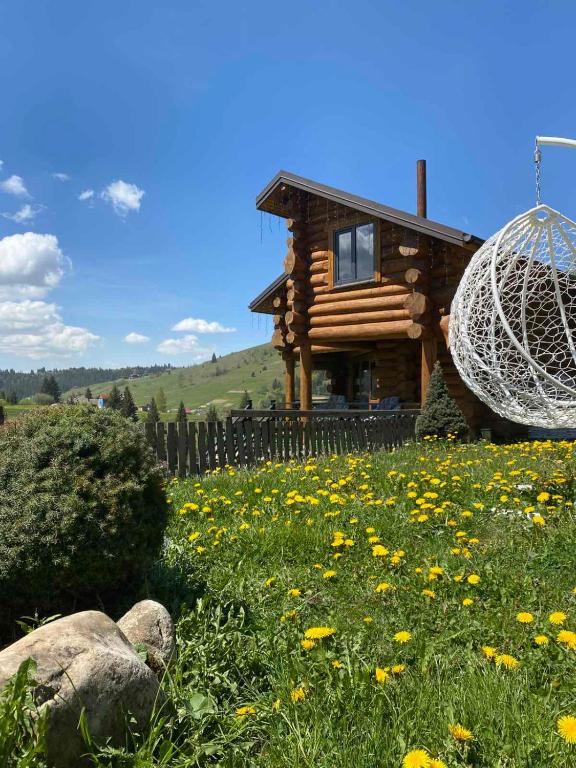 a log cabin with a field of flowers in front of a house at Villa Filiak in Yablunytsya