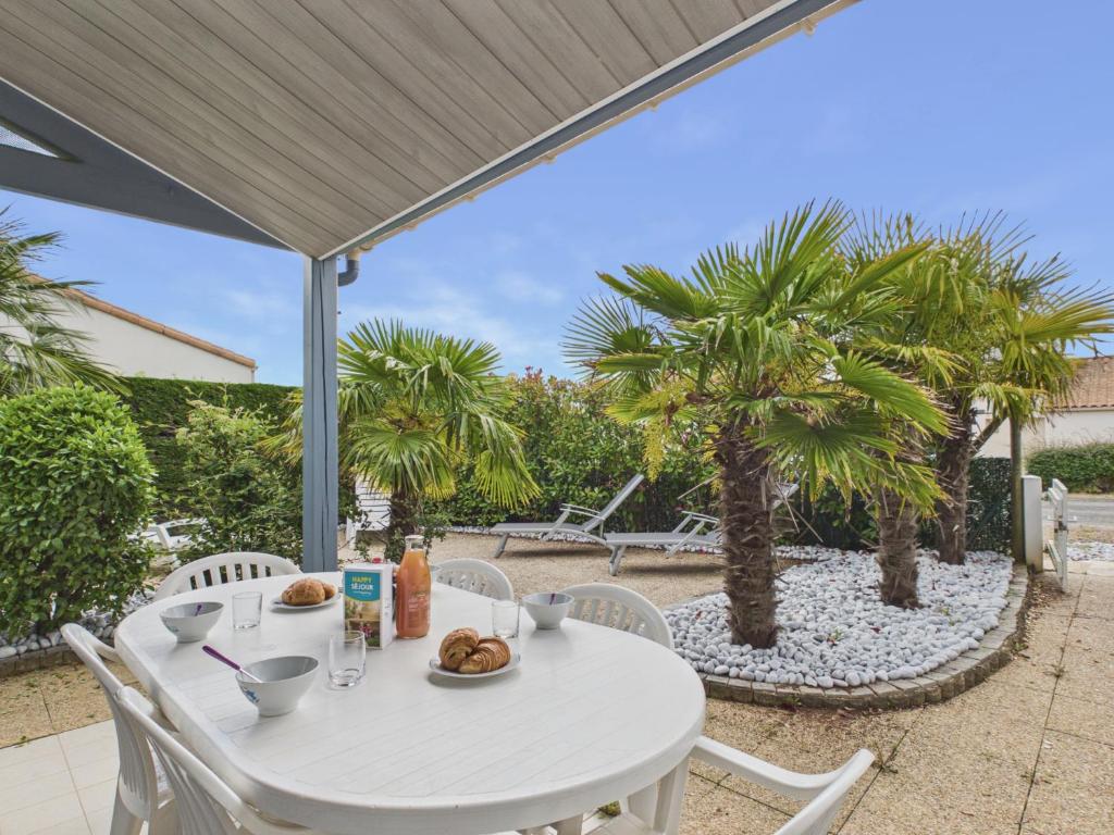 a white table and chairs on a patio with palm trees at La Tranche-sur-Mer, maison pour 3 adultes-2 enfants in La Tranche-sur-Mer