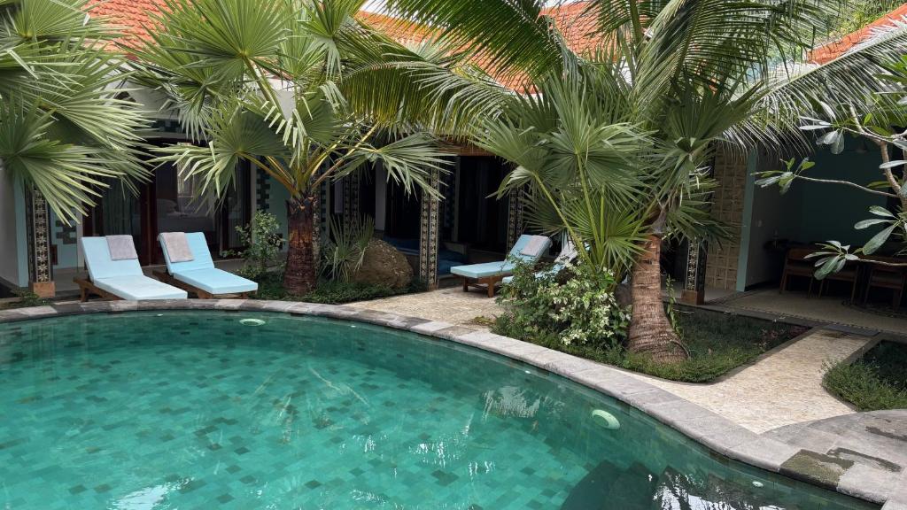 a swimming pool with two chairs and palm trees at ABG Villas - Agrowisata Amed in Amed