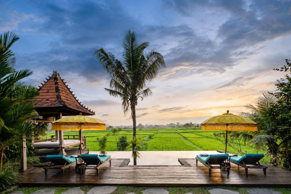 a resort with a pool with chairs and umbrellas at The Joglo at Umah Sunset in Ubud