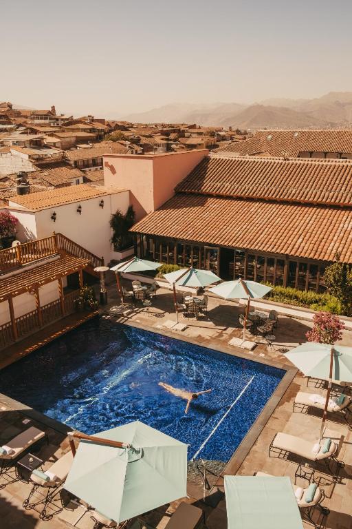 a pool with chairs and umbrellas and a person swimming at Palacio Nazarenas, A Belmond Hotel, Cusco in Cusco