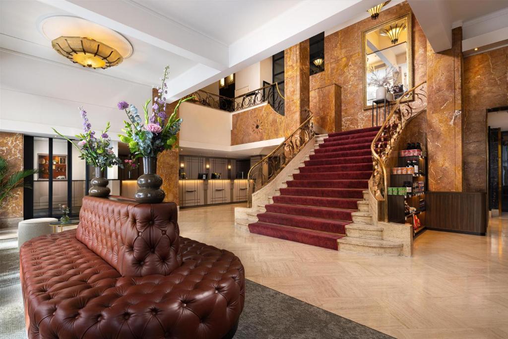 eine Lobby mit Treppe und braunem Ledersofa in der Unterkunft NH Atlanta Rotterdam Hotel in Rotterdam