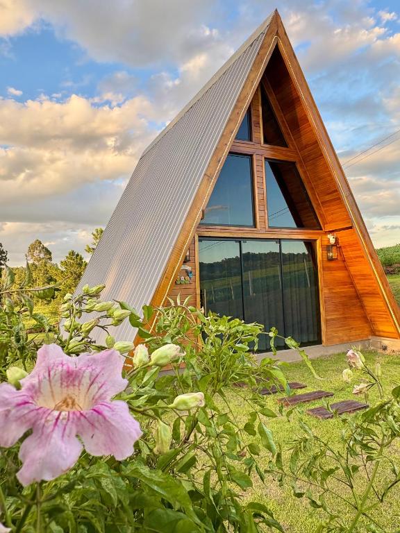 a small house with a pitched roof and flowers at Sítio das Amoreiras- Cabana in Tabapira