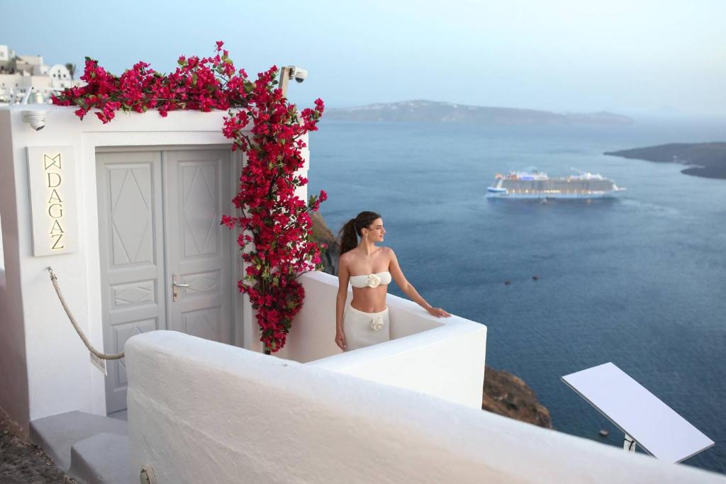 a woman standing on the side of a door with flowers at Dagaz Suites in Fira