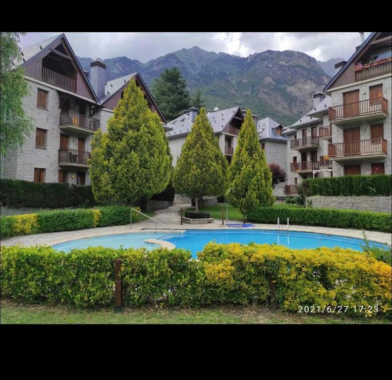 a large swimming pool in a courtyard with trees and buildings at La Buhardilla - Benasque in Benasque