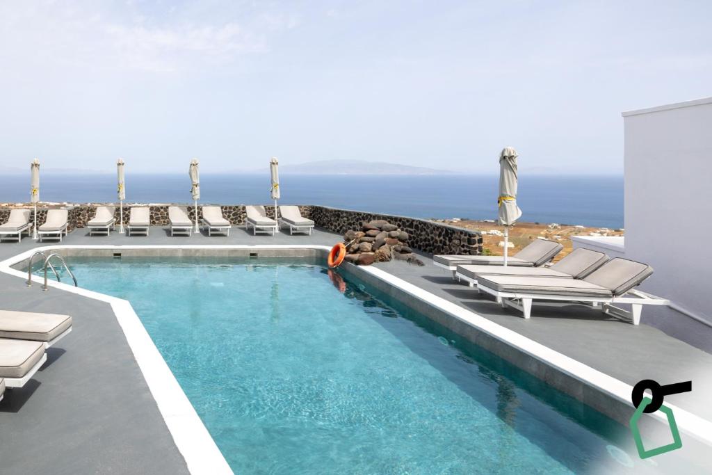 a pool with lounge chairs and the ocean in the background at Hotiday Santorini Seafront in Santorini