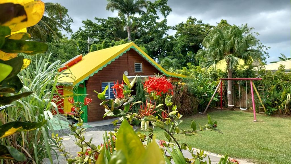 a small house with a yellow roof in a garden at Méline in Baie-Mahault