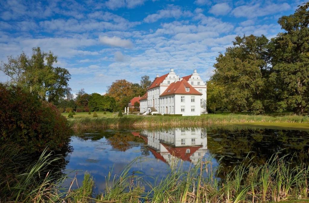 a large white house with a red roof reflected in a pond at Ferienwohnung Herrenhaus Linker Seitenflügel II - Boldevitzer Rügenkaten in Parchtitz