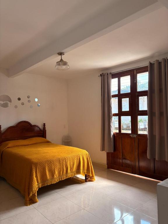 a bedroom with a bed with a yellow bedspread and a window at La casa de los Faroles in Cuetzalán del Progreso