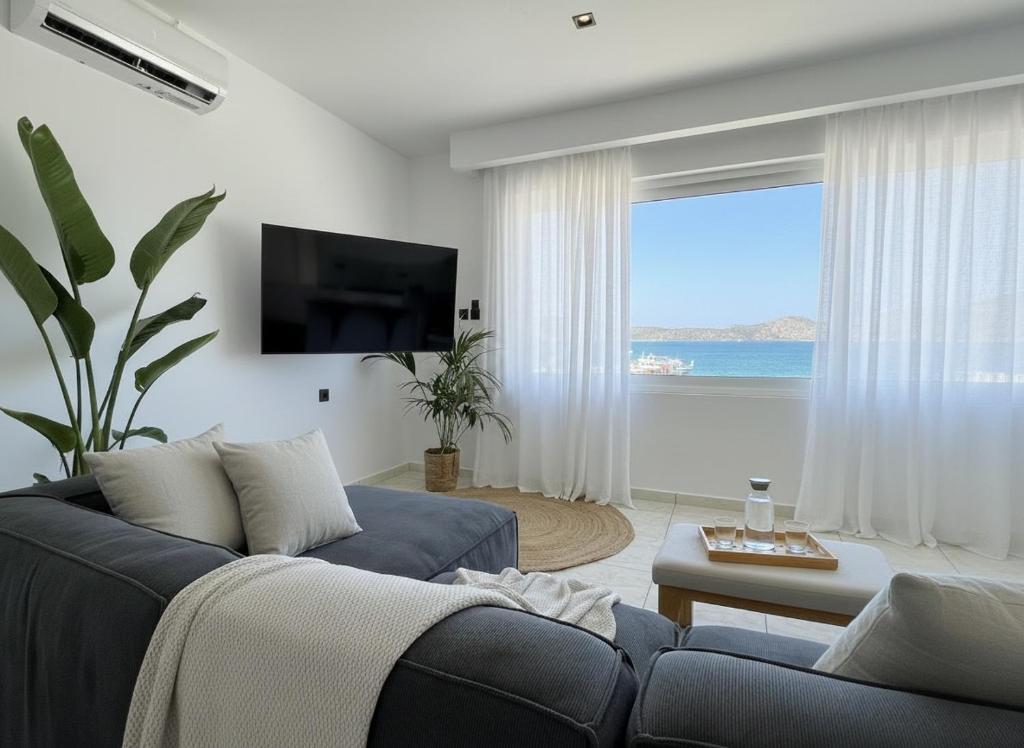 a living room with a blue couch and a large window at Elounda Port Apartment in Elounda