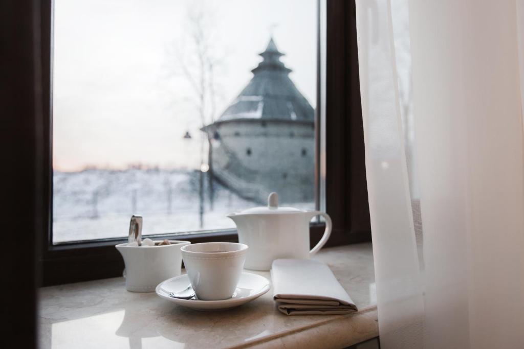 a table with tea cups and a window with a lighthouse at Hotel Pokrovsky in Pskov