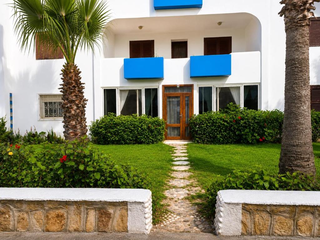a white house with blue windows and a palm tree at Plage al amin eden in Fnidek