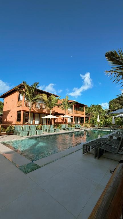 a resort with a pool with chairs and a building at Vila Anambé in Uruçuca