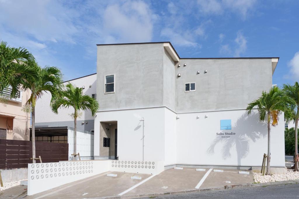 a white building with palm trees in front of it at Solis Studio Miyako SeaSide in Miyako-jima