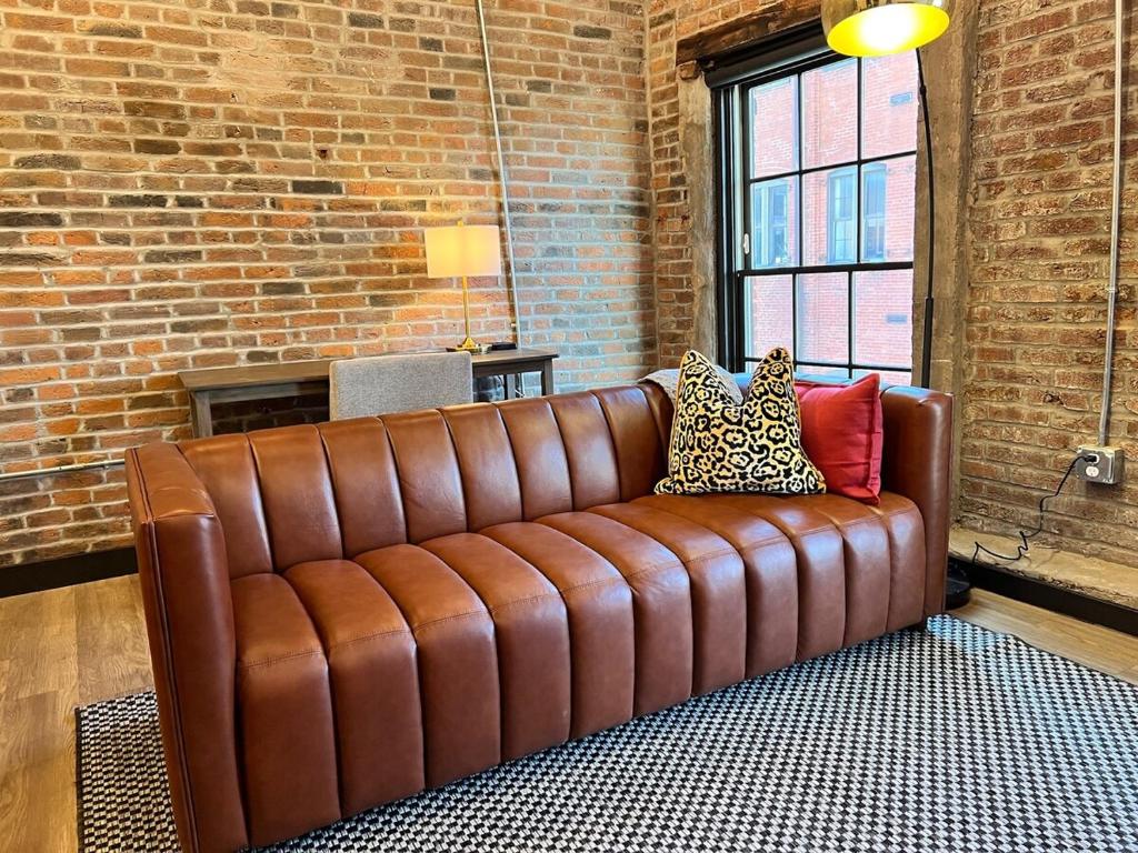 a brown leather couch in a room with a brick wall at Brick & Bed Riverfront Lofts, T 308 in Saint Louis