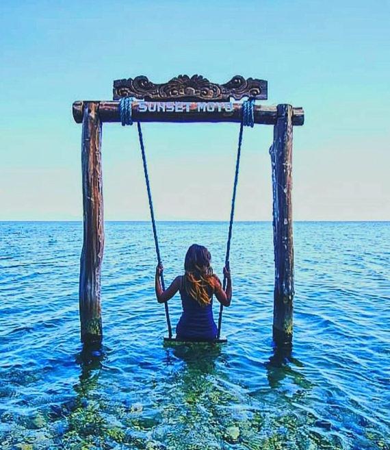 a woman sitting on a swing in the water at Sunset Moyo Bungalows in Moyo Island
