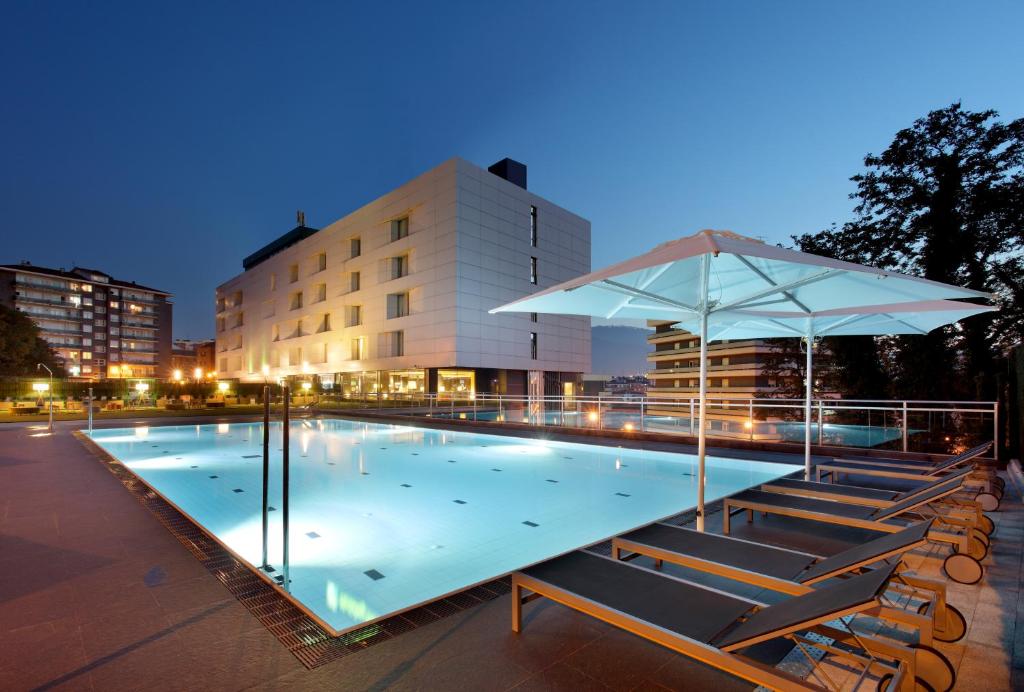 a swimming pool with chairs and an umbrella at Occidental Bilbao in Bilbao