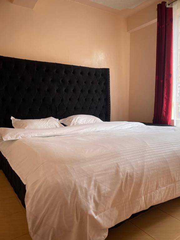 a bedroom with a white bed with a black headboard at Nadine's Enclave in Kisii
