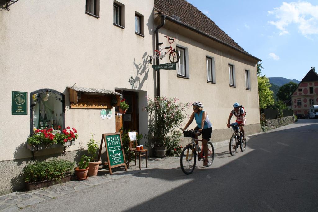 two people riding bikes down a street next to a building at Weinbau-Gästezimmer Martin und Eva Maria Jamek in Weissenkirchen in der Wachau
