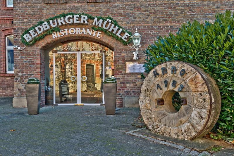 un bâtiment avec une grande roue en bois devant une porte dans l'établissement Hotel Bedburger Mühle, à Bedburg