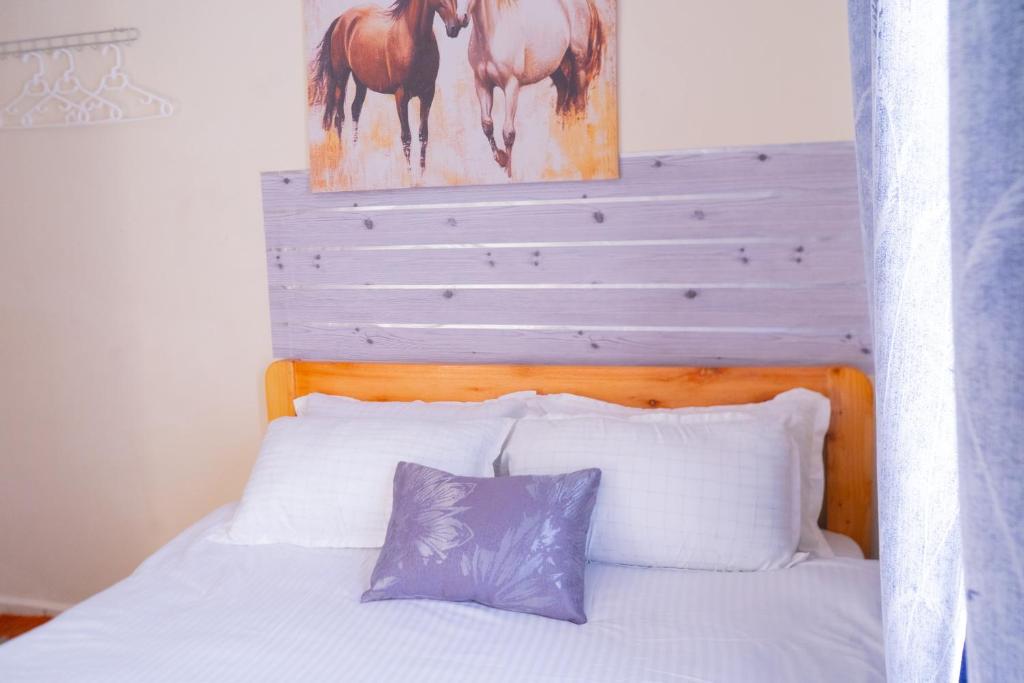 a bed with white pillows and a painting of horses at Benson waweru APPARTMENT in Kakamega