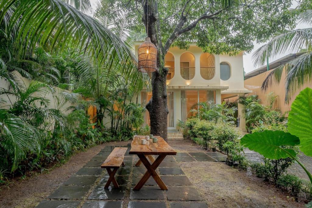 a wooden table in front of a house with a tree at SaffronStays Oslo in Anjuna