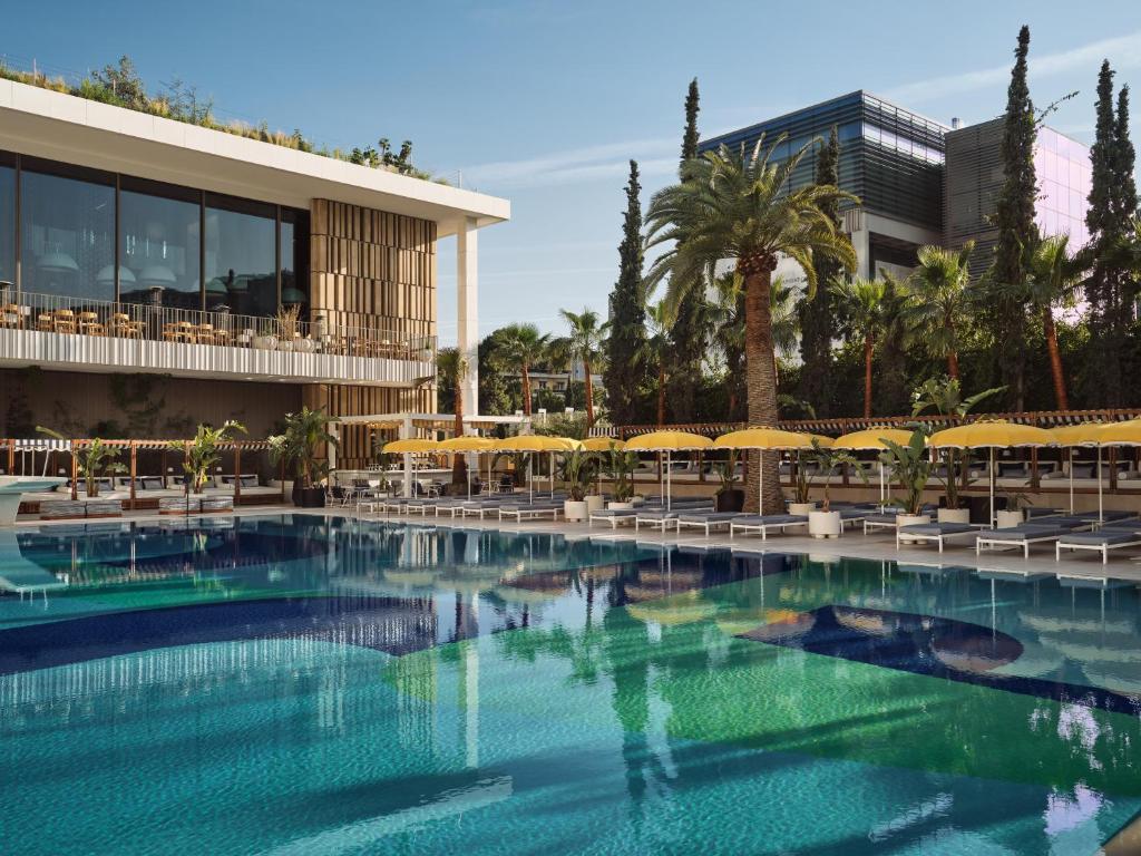 a swimming pool with umbrellas and chairs and a building at Conrad Athens The Ilisian in Athens