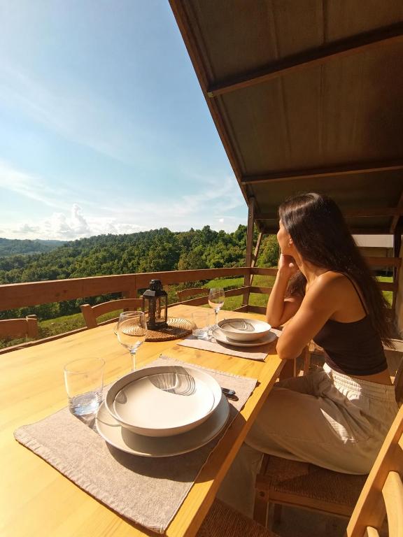 a woman sitting at a wooden table with plates and wine glasses at Glamping Podere Poggiagrilli in San Gervasio