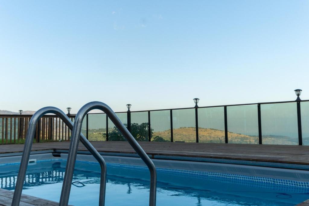 a swimming pool with a wooden deck and a railing at Velen Harmony- בקתות מושלמות עם בריכה במתחם in ‘Ein el Asad
