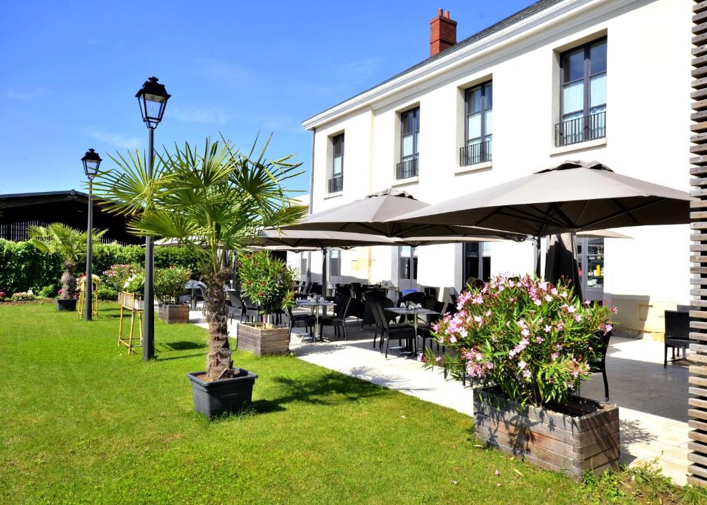 un patio con mesas y sombrillas frente a un edificio en AUBERGE DU CHÂTEAU BLEU en Tremblay En France